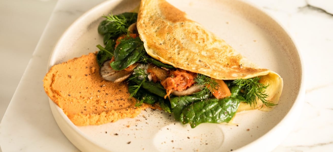 a fluffy golden omelette stuffed with fresh vegetables, served on an off-white plate, garnished with herbs